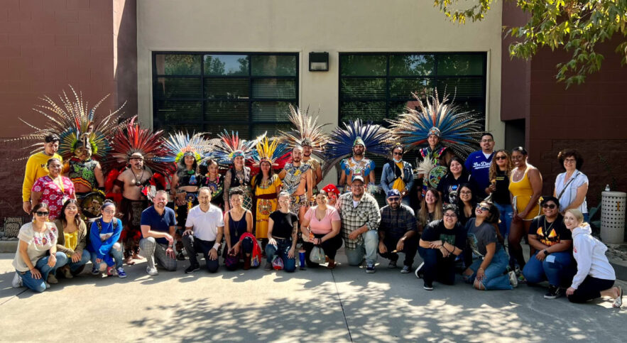 large group of people smiling with some dressed in feathered head dresses