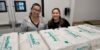 Two people smile for the camera while behind packages of Baby2Baby diapers.