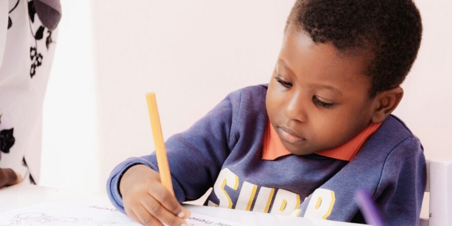 Small child writing in a notebook with a pencil.